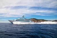 Luxurious Devonport yacht cruising near rocky coastline under clear blue sky, 2014 model.
