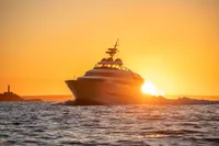 Luxury Devonport yacht sailing at sunset, 2014, with lighthouse silhouette in the background.