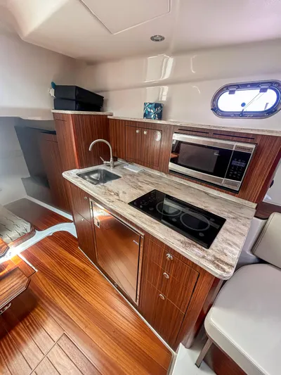  Yacht Photos Pics 2018 Pursuit OS 355 Offshore yacht interior with kitchenette, featuring wood cabinetry and modern appliances.