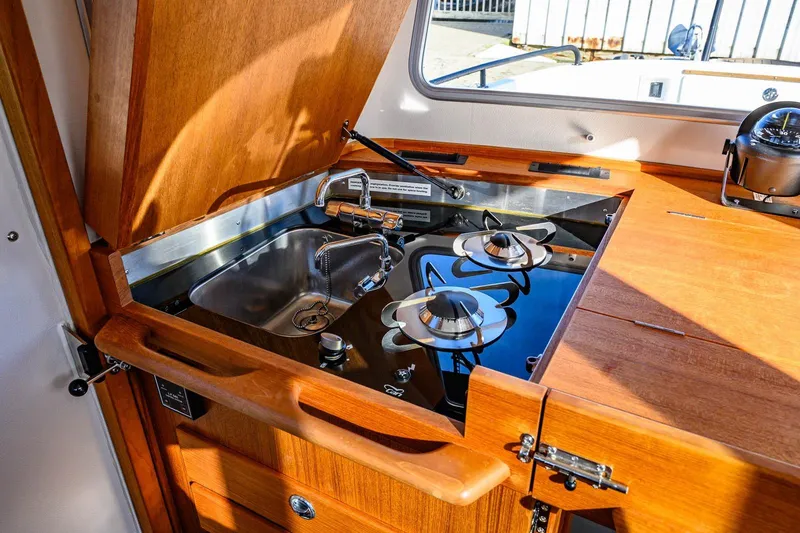  Yacht Photos Pics 2023 Targa 27.2 boat kitchen with stove and sink, featuring wooden cabinetry.