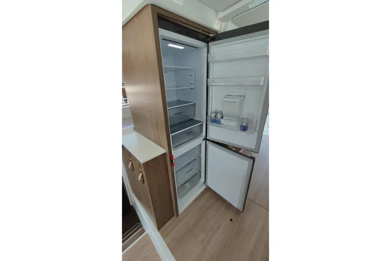  Yacht Photos Pics Open refrigerator in Bali 4.2 model, 2023, with wooden paneling and organized interior shelves.