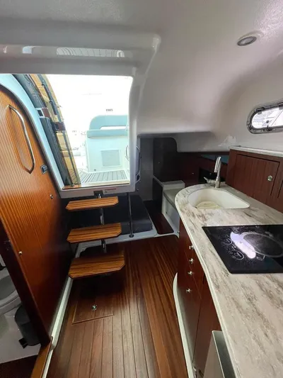 No Name Yacht Photos Pics 2019 Pursuit OS 385 Offshore interior with wooden flooring, kitchenette, and steps leading to deck.