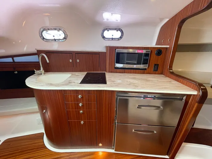 No Name Yacht Photos Pics 2019 Pursuit OS 385 Offshore yacht kitchen with wood cabinetry, sink, stove, microwave, and stainless steel appliances.
