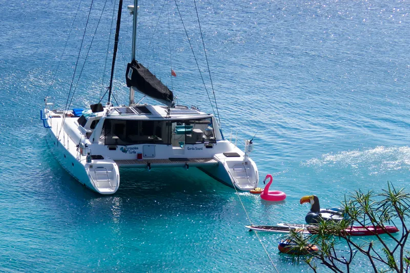 Turquoise Turtle Yacht Photos Pics Catamaran Voyage 500 (2001) anchored in clear blue water with inflatable toys nearby.