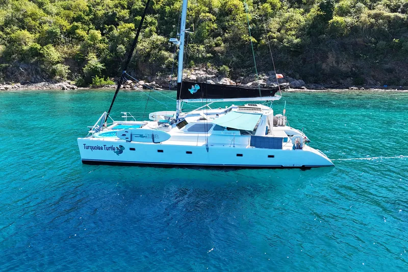 Turquoise Turtle Yacht Photos Pics Catamaran "Turquoise Turtle" Voyage 500, 2001, anchored in clear blue water near lush coastline.