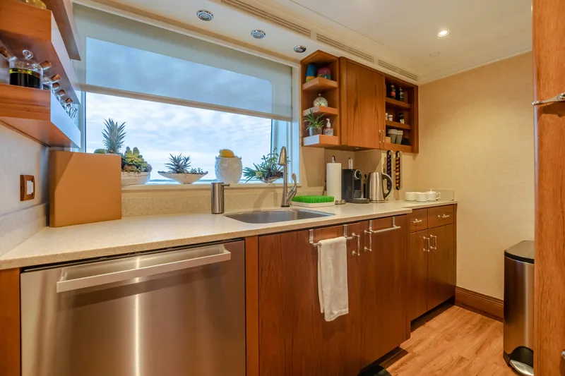Shadowl Yacht Photos Pics Modern yacht kitchen with wooden cabinets, stainless steel appliances, and decorative plants by the window.