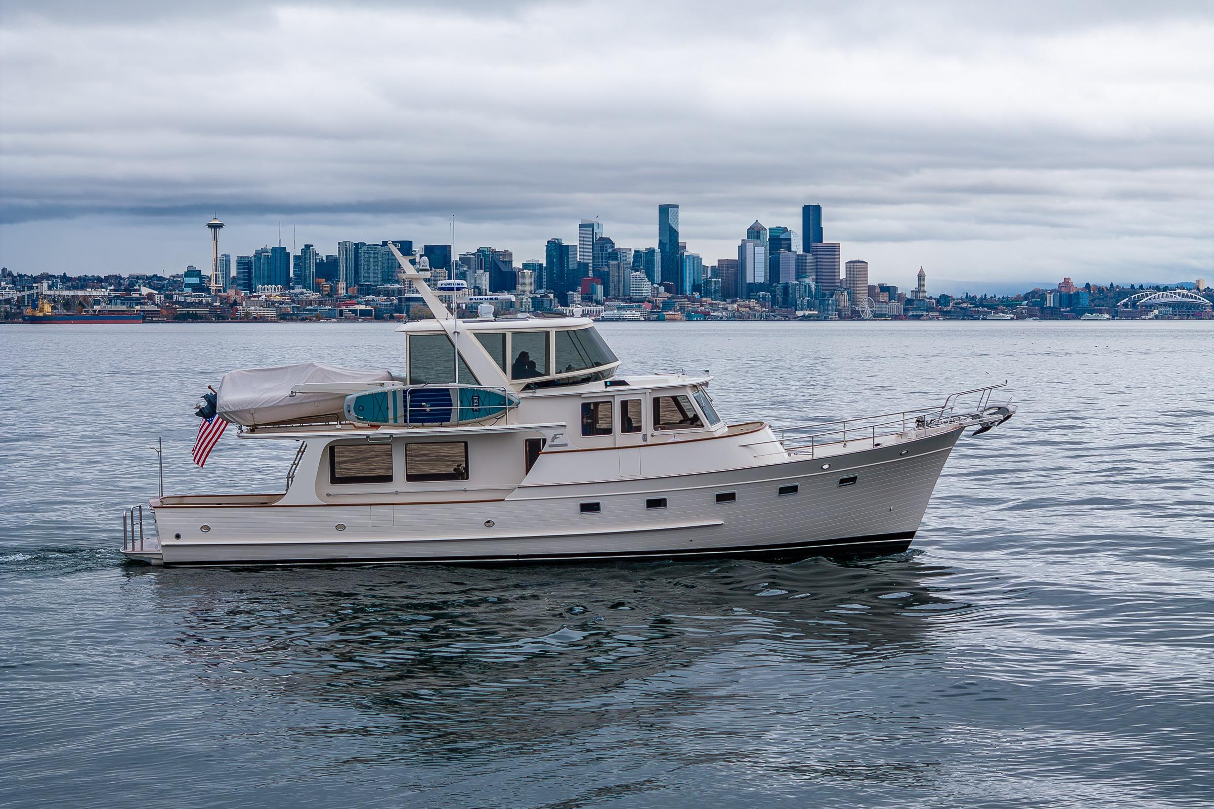 2026 Fleming 55 Pilothouse yacht cruising near Seattle skyline on a cloudy day.