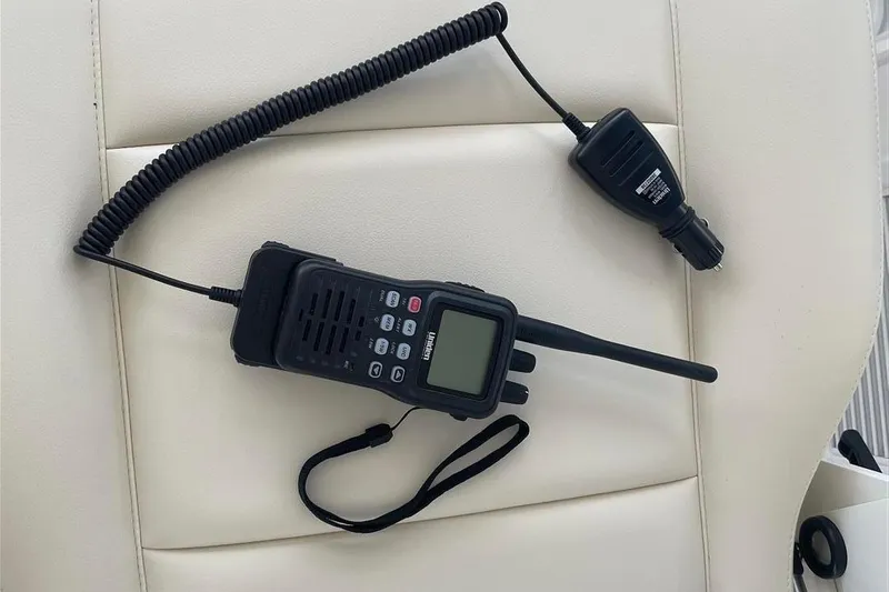 O-m-g Yacht Photos Pics Handheld radio on white seat, MJM 3, 2023 model, with coiled cord and microphone.