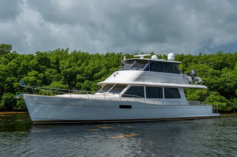 Painkiller Yacht Photos Pics 2023 Grand Banks GB60 yacht on water, surrounded by lush greenery.