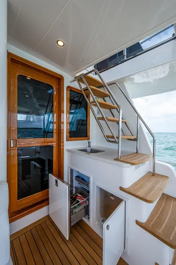 Painkiller Yacht Photos Pics 2023 Grand Banks GB60 yacht interior with wooden stairs, open cabinets, and ocean view.