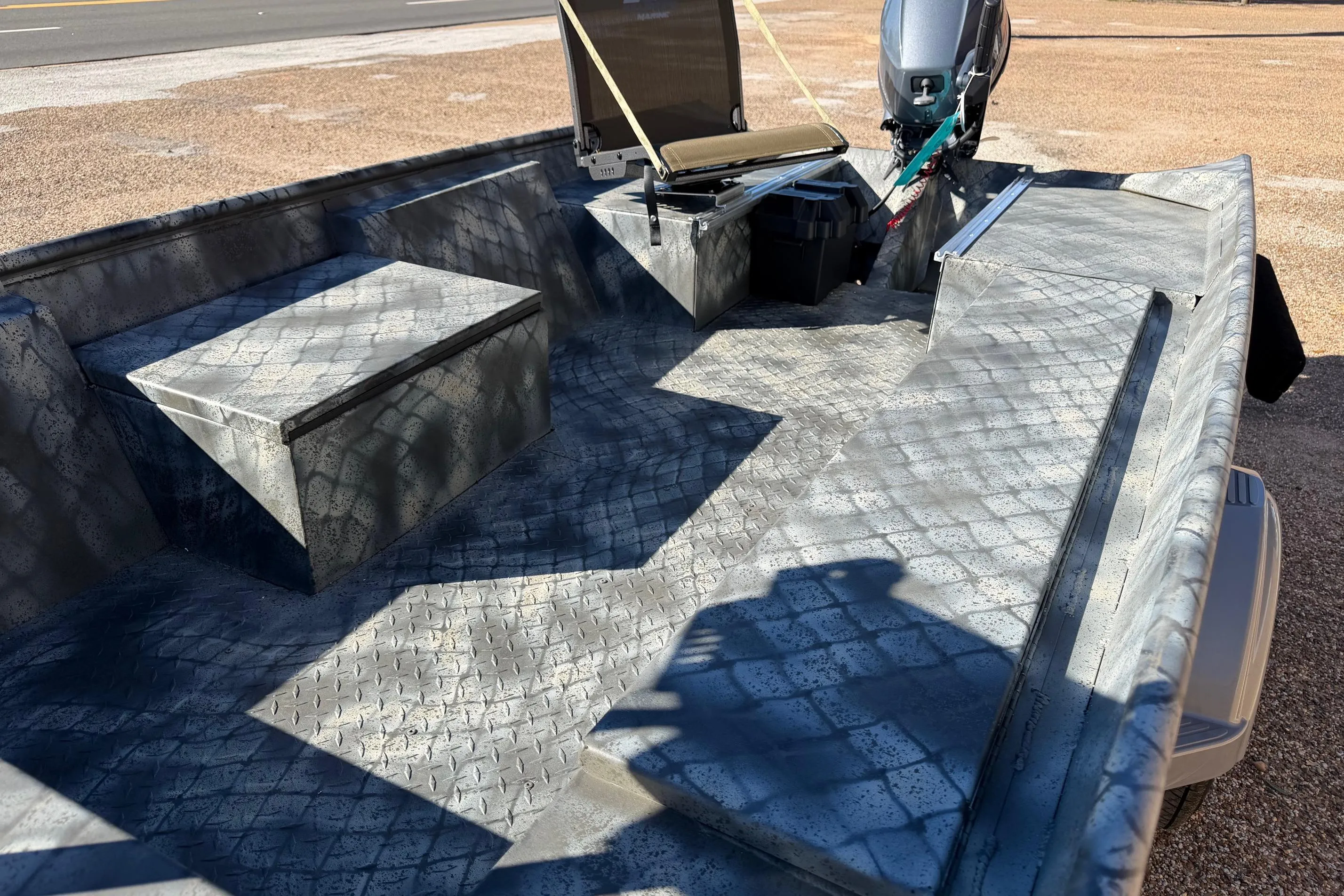 2025 WeldBilt 1448 boat interior with textured flooring and motor, parked on gravel.