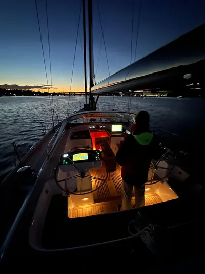 Pinnacle Yacht Photos Pics 2023 Hallberg-Rassy 57 yacht sailing at dusk with illuminated cockpit and serene waters.