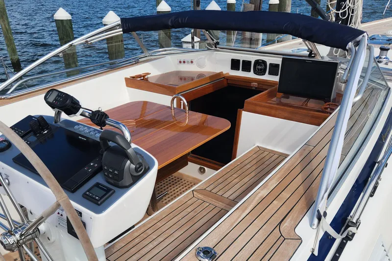 Pinnacle Yacht Photos Pics 2023 Hallberg-Rassy 57 yacht cockpit with wooden table, steering wheel, and navigation equipment.