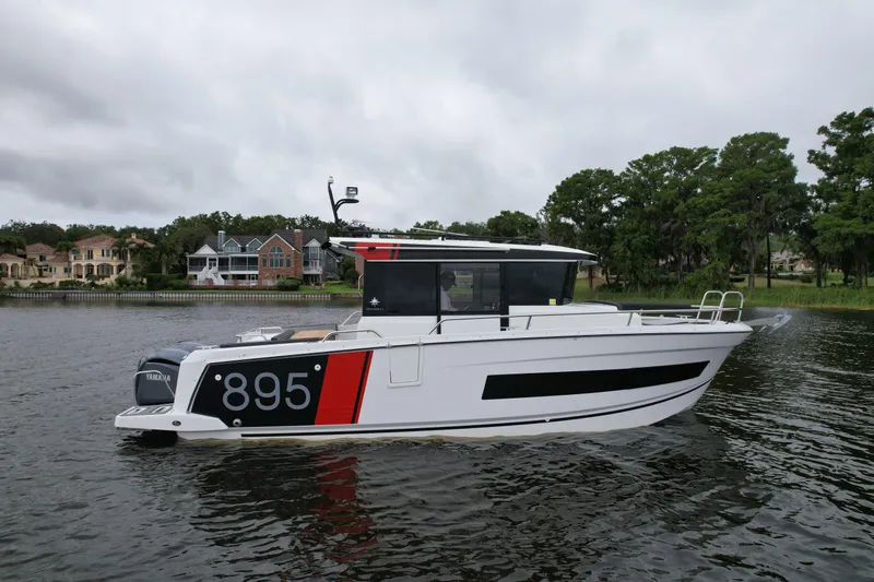  Yacht Photos Pics 2023 Jeanneau NC Sport 895 boat on a calm lake with houses in the background.