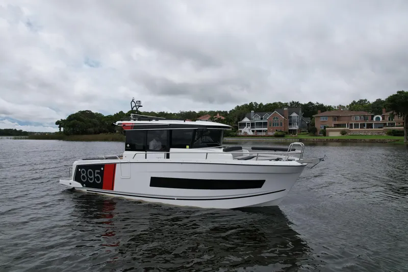  Yacht Photos Pics 2023 Jeanneau NC Sport 895 boat on a calm river near waterfront homes.