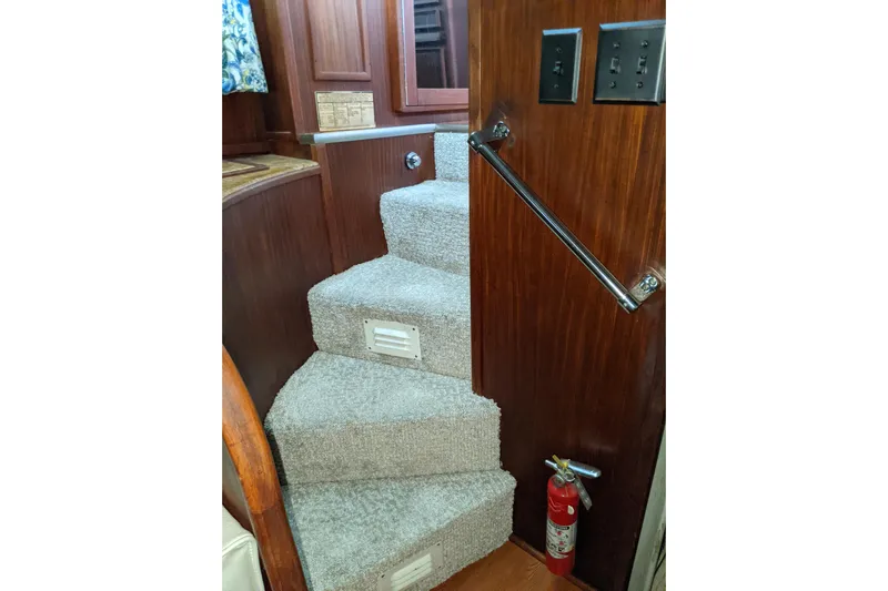 Sky To Sea Yacht Photos Pics Carpeted stairs inside 1984 Hatteras 53 Motor Yacht with wooden paneling and fire extinguisher.