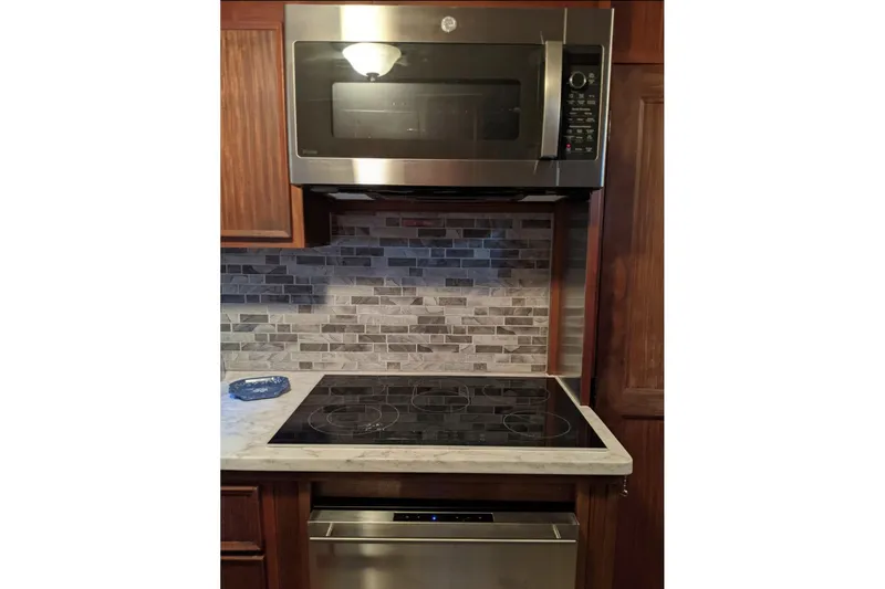 Sky To Sea Yacht Photos Pics Modern kitchen with stainless steel microwave, electric cooktop, and tiled backsplash on a yacht.