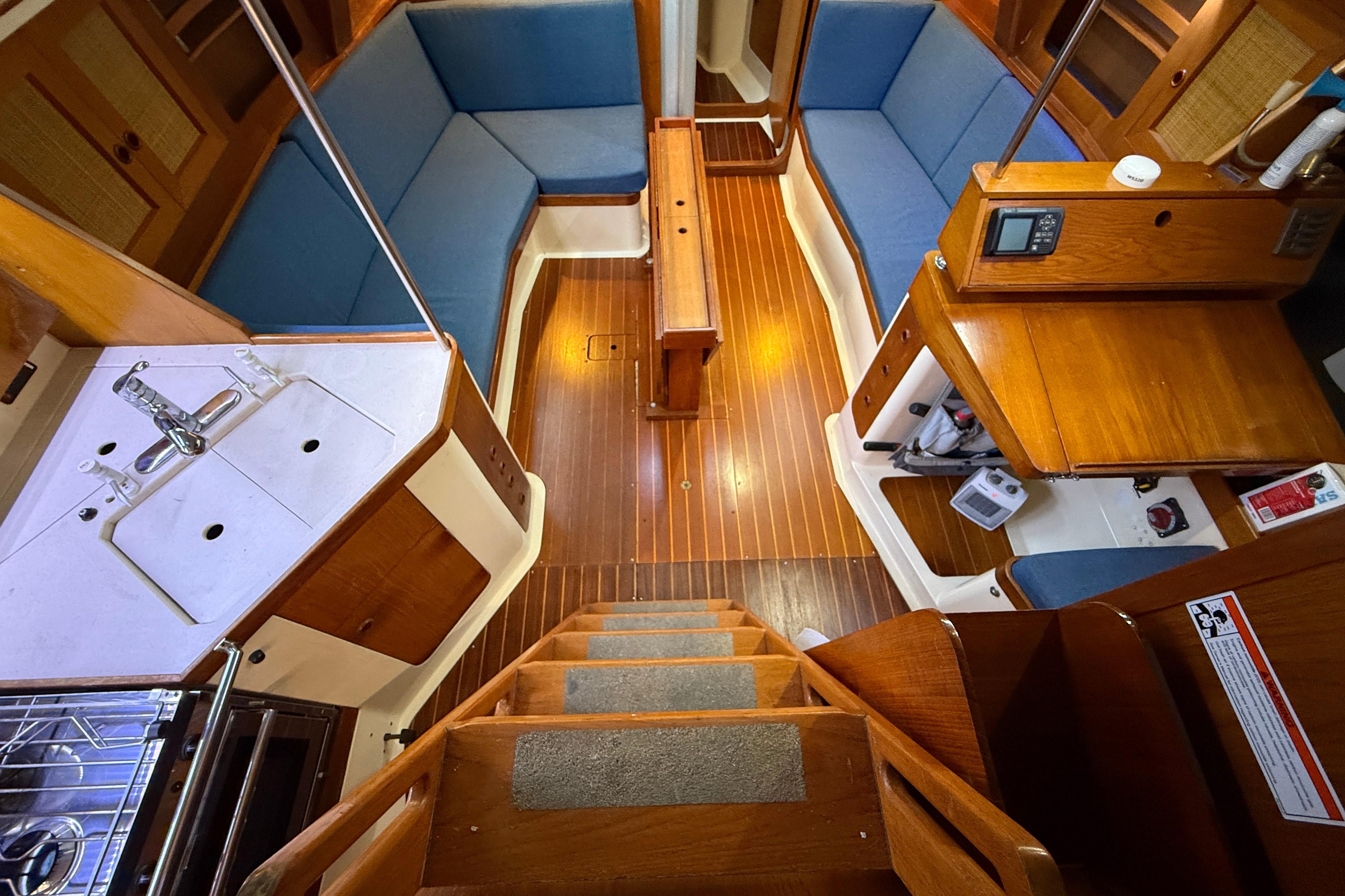 Interior of a 1987 CS 40 sailboat, featuring wooden flooring and blue cushioned seating.