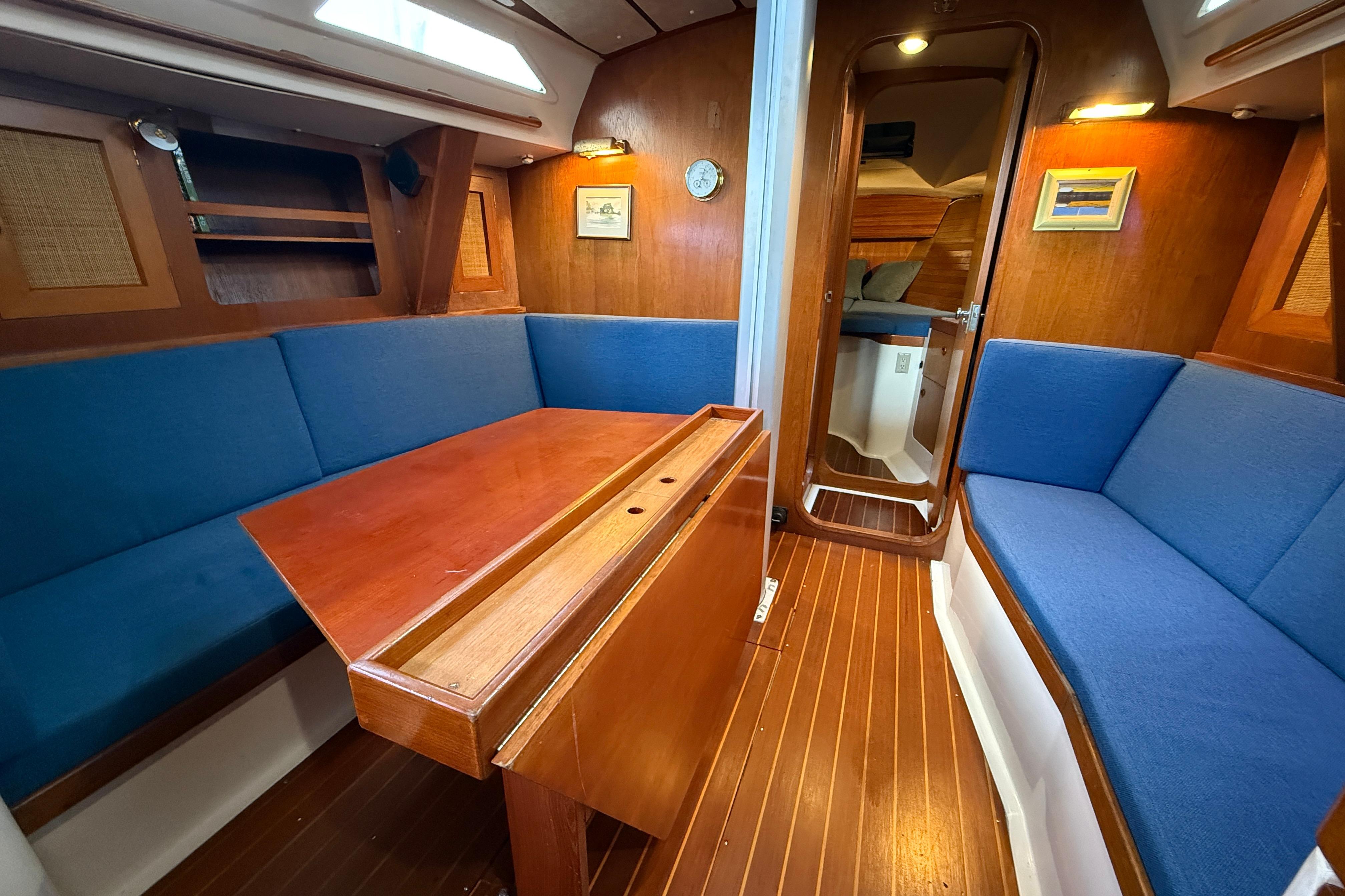1987 CS 40 yacht interior with blue seating, wooden table, and cozy cabin atmosphere.