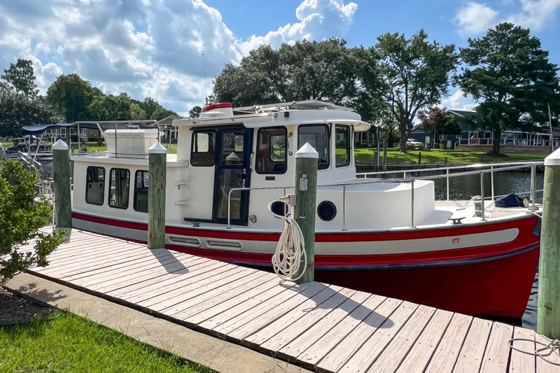 Mirage Yacht Photos Pics Red and white 1999 Nordic 32 boat docked by a wooden pier under a partly cloudy sky.
