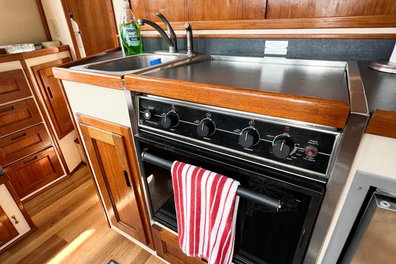 Mirage Yacht Photos Pics Compact kitchen area in a 1999 Nordic 32 boat with stove, sink, and wooden cabinetry.
