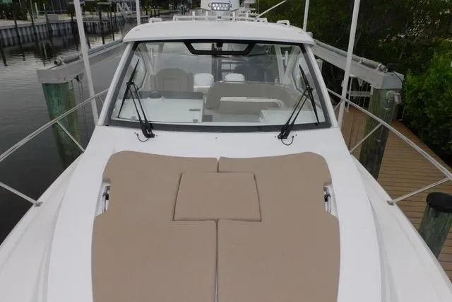  Yacht Photos Pics 2019 Pursuit OS 325 Offshore boat with beige deck cushions, docked near greenery.