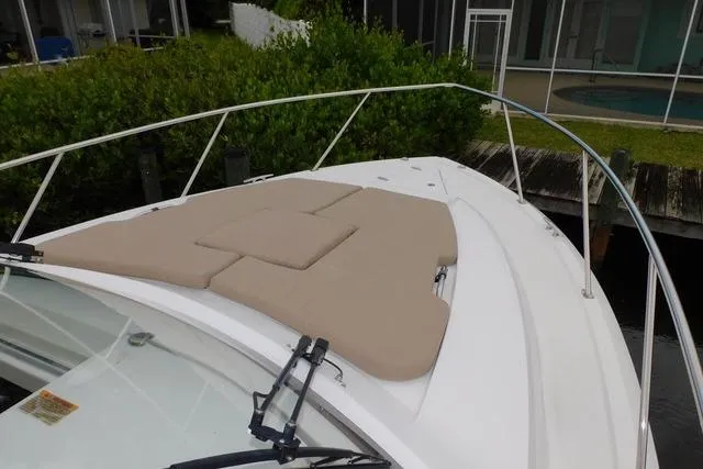  Yacht Photos Pics 2019 Pursuit OS 325 Offshore boat with cushioned bow deck, docked near greenery.