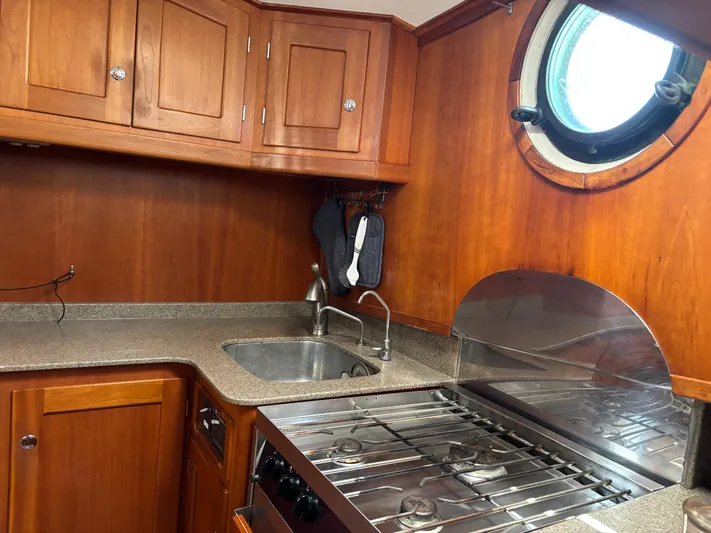 Diesel Duck Yacht Photos Pics 1999 Diesel Duck Trawler kitchen with wooden cabinets, stainless steel sink, and stove under a porthole.