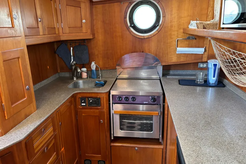 Diesel Duck Yacht Photos Pics 1999 Diesel Duck Trawler kitchen with wooden cabinets, stove, and porthole window.