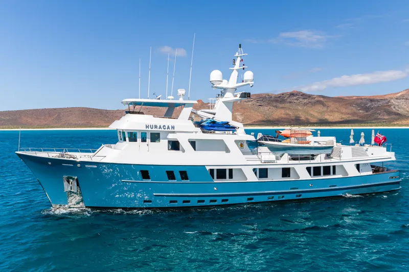 Huracan Yacht Photos Pics Delta Marine Expedition yacht, 1991 model, cruising in clear blue waters near a scenic coastline.