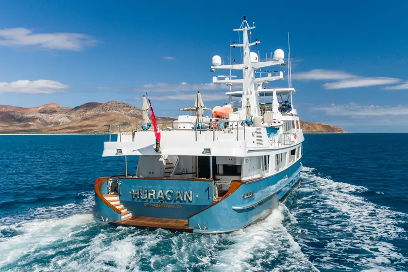 Huracan Yacht Photos Pics Delta Marine Expedition yacht from 1991 cruising in clear blue waters near rocky coastline.