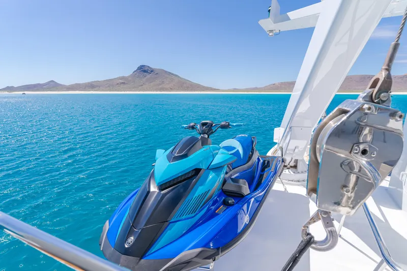 Huracan Yacht Photos Pics Blue jet ski on Delta Marine Expedition yacht, 1991, with scenic ocean and mountain backdrop.