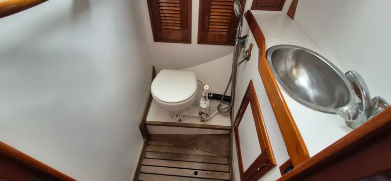 Blue Skies Yacht Photos Pics Compact bathroom in 1990 Able Chuck Paine Sloop with toilet, sink, and wooden accents.