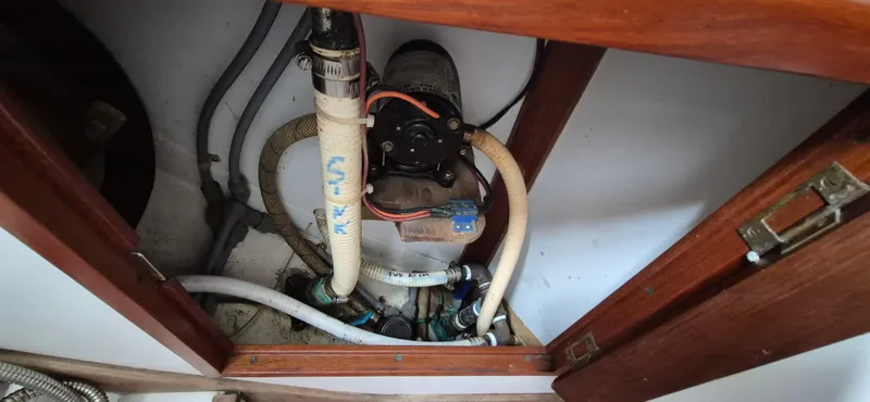 Blue Skies Yacht Photos Pics Bilge pump system inside 1990 Able Chuck Paine Sloop, featuring hoses and wooden cabinetry.