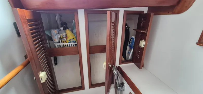 Blue Skies Yacht Photos Pics Wooden cabinets inside a 1990 Able Chuck Paine Sloop, storing cleaning supplies and essentials.