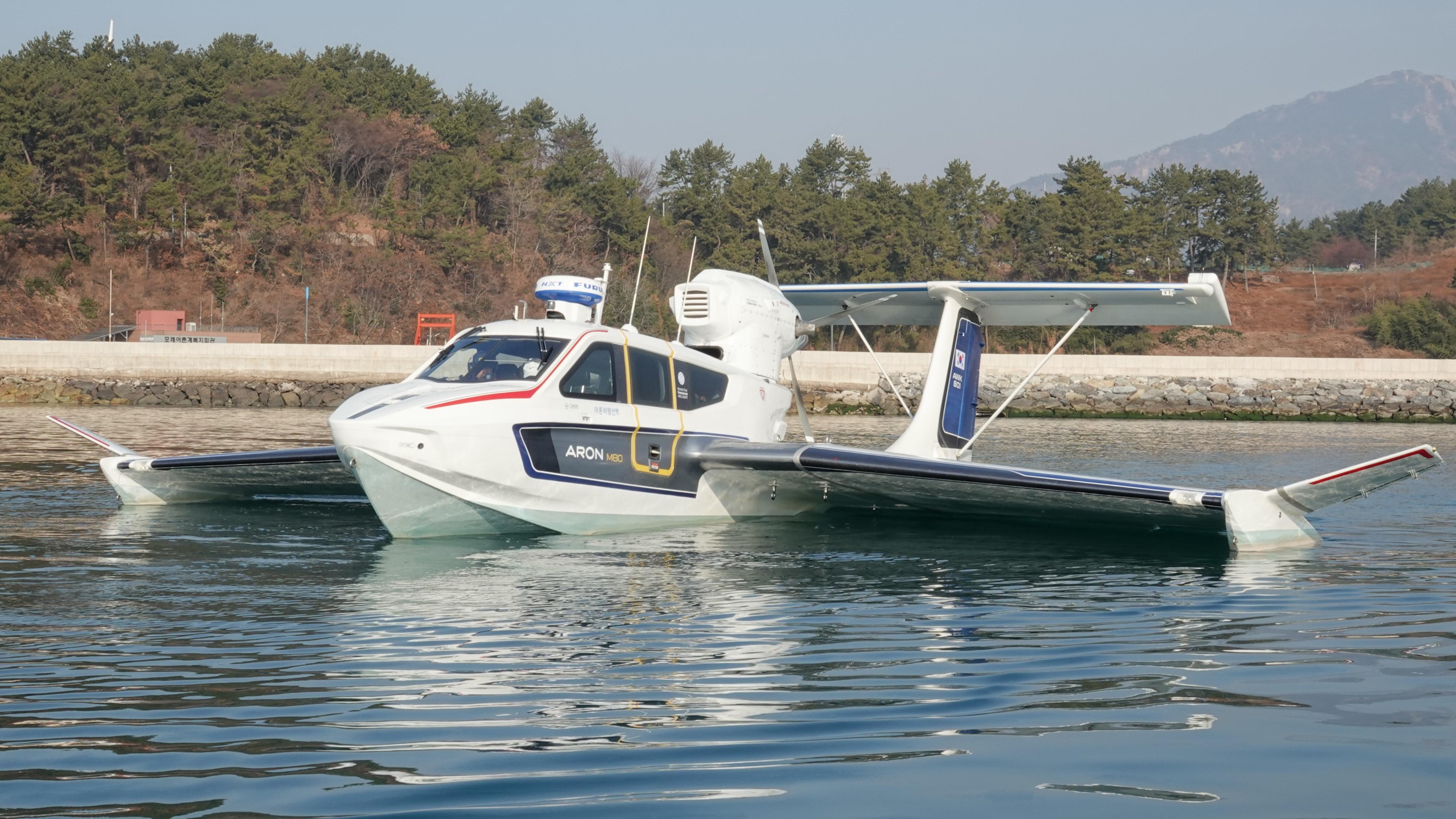 2025 Aron M 80 seaplane on calm water, surrounded by trees and mountains.