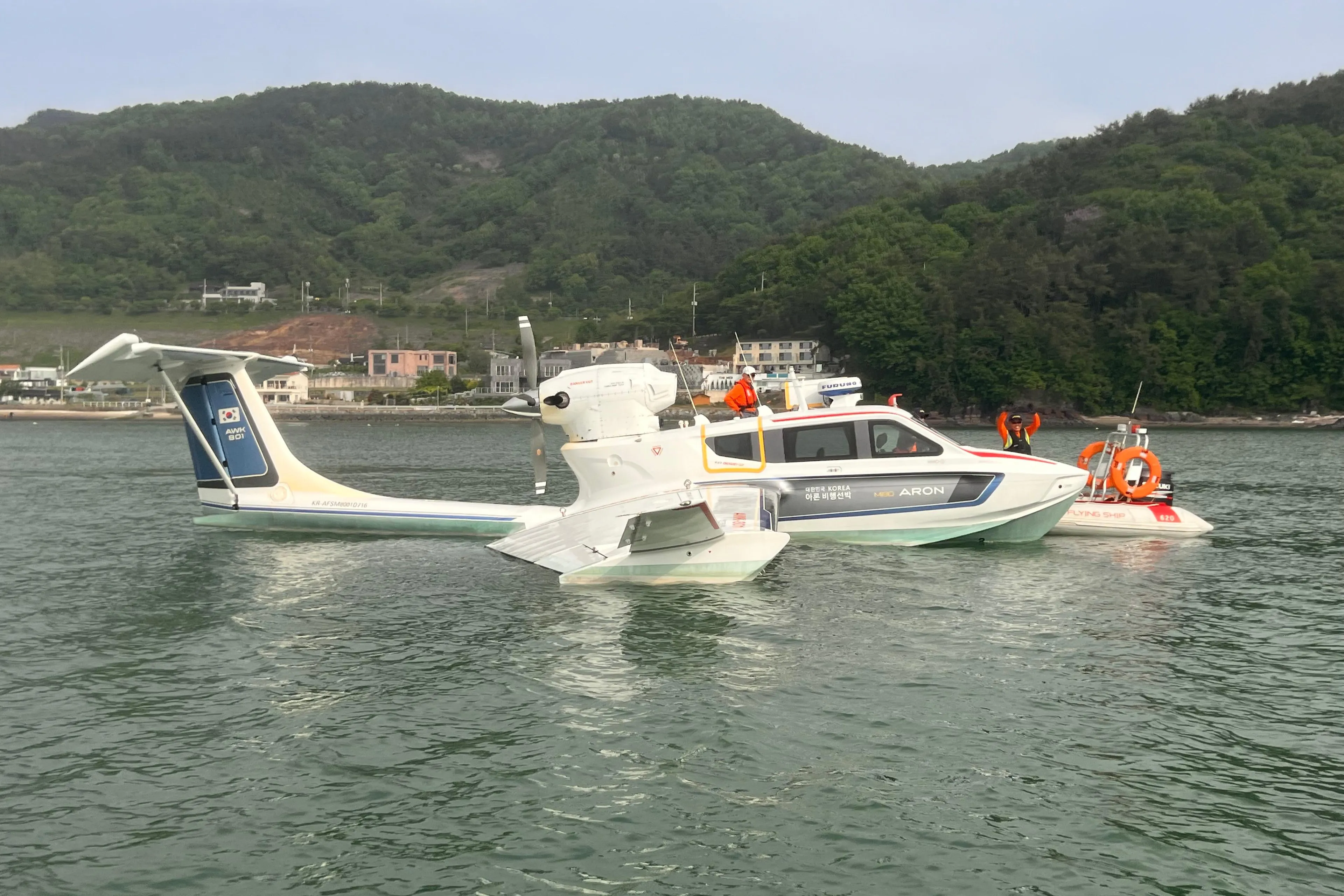 Futuristic Aron M 80 seaplane on water, 2025 model, with scenic mountain backdrop.