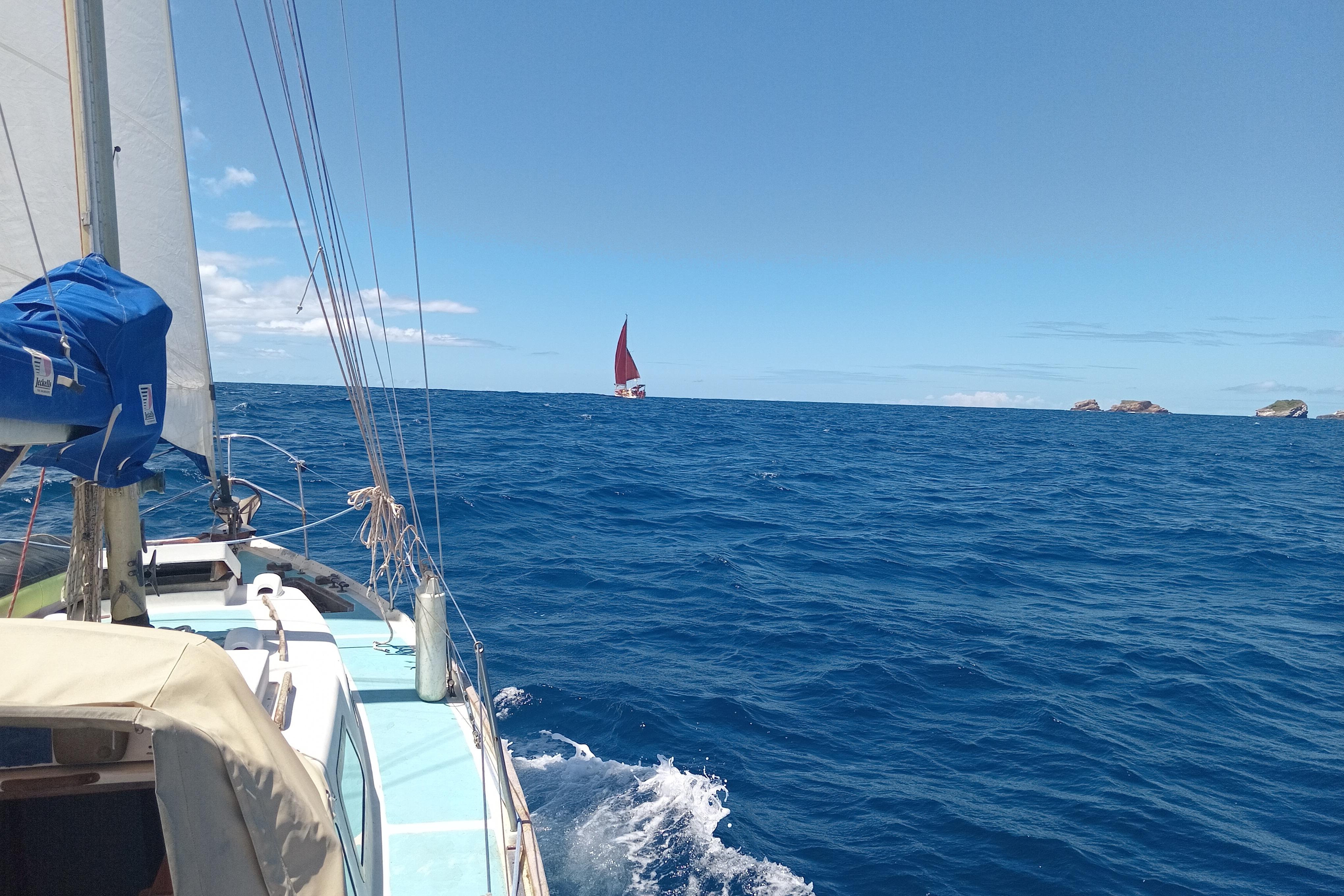 Sailing on a 1965 Nicholson 32 yacht in open blue sea, distant red sail visible.