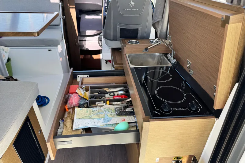 Yacht Photos Pics 2019 Jeanneau NC 895 interior kitchen with stove, sink, and open drawer with tools and map.