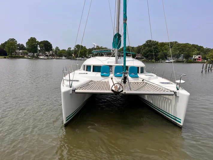 Wayward Sun Yacht Photos Pics Lagoon 380 catamaran, 2000 model, anchored on calm water with lush greenery in the background.