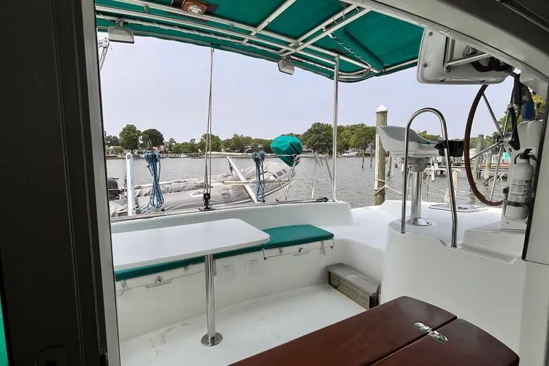Wayward Sun Yacht Photos Pics Lagoon 380 catamaran cockpit with green canopy, docked by a serene waterfront.