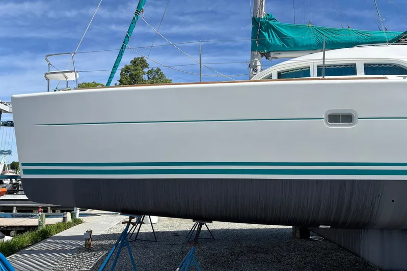 Wayward Sun Yacht Photos Pics 2000 Lagoon 380 catamaran on stands, white hull with teal accents, clear sky background.