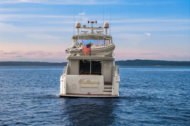 Bellissimo Yacht Photos Pics 2001 Hatteras 63 Cockpit Motor Yacht on serene water, rear view with American flag.