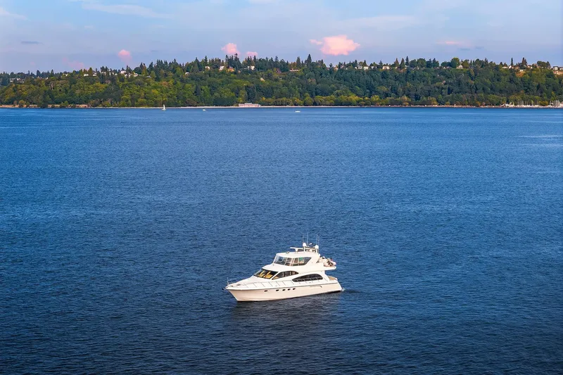 Bellissimo Yacht Photos Pics 2001 Hatteras 63 Cockpit Motor Yacht on serene blue water with lush green shoreline.