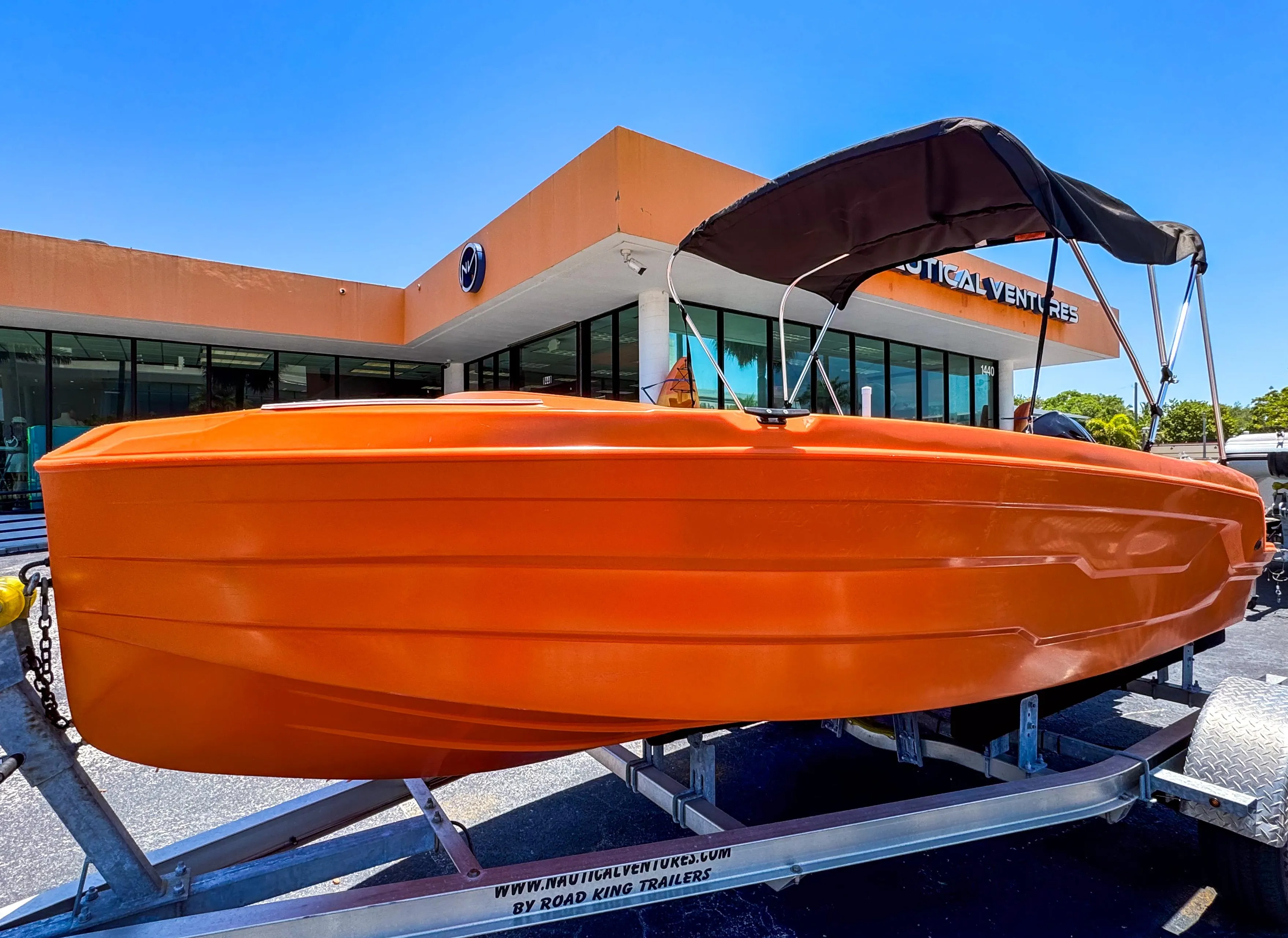 2024 Vision Marine Technologies Phantom boat, orange hull, on trailer outside a building.