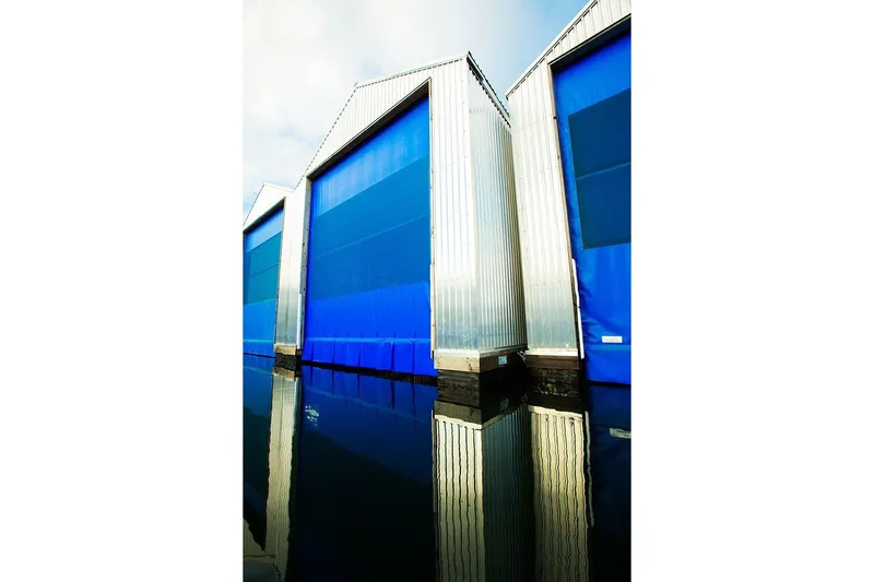  Yacht Photos Pics Modern 2025 Custom OBMG Boathouse with blue doors reflecting on water.