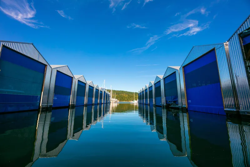  Yacht Photos Pics Modern OBMG Boathouse 2025 with blue doors reflecting on calm water under clear sky.