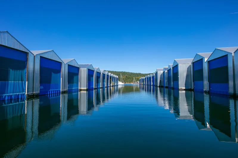 Yacht Photos Pics Modern boathouses reflecting on calm water under clear blue sky, Custom OBMG Boathouse 2025.