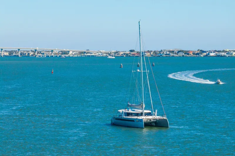 Gtfo Yacht Photos Pics 2024 Balance 482 catamaran sailing on a calm blue sea near a coastal bridge.
