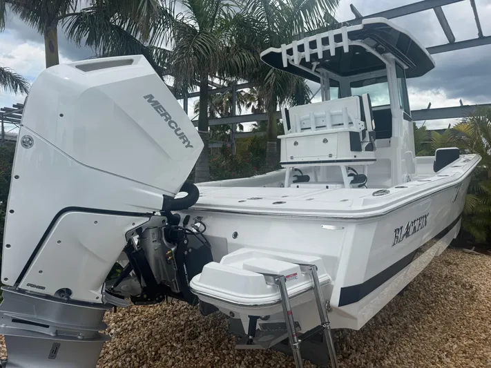  Yacht Photos Pics 2026 Blackfin 262 HB boat with Mercury engine, parked on gravel, surrounded by palm trees.